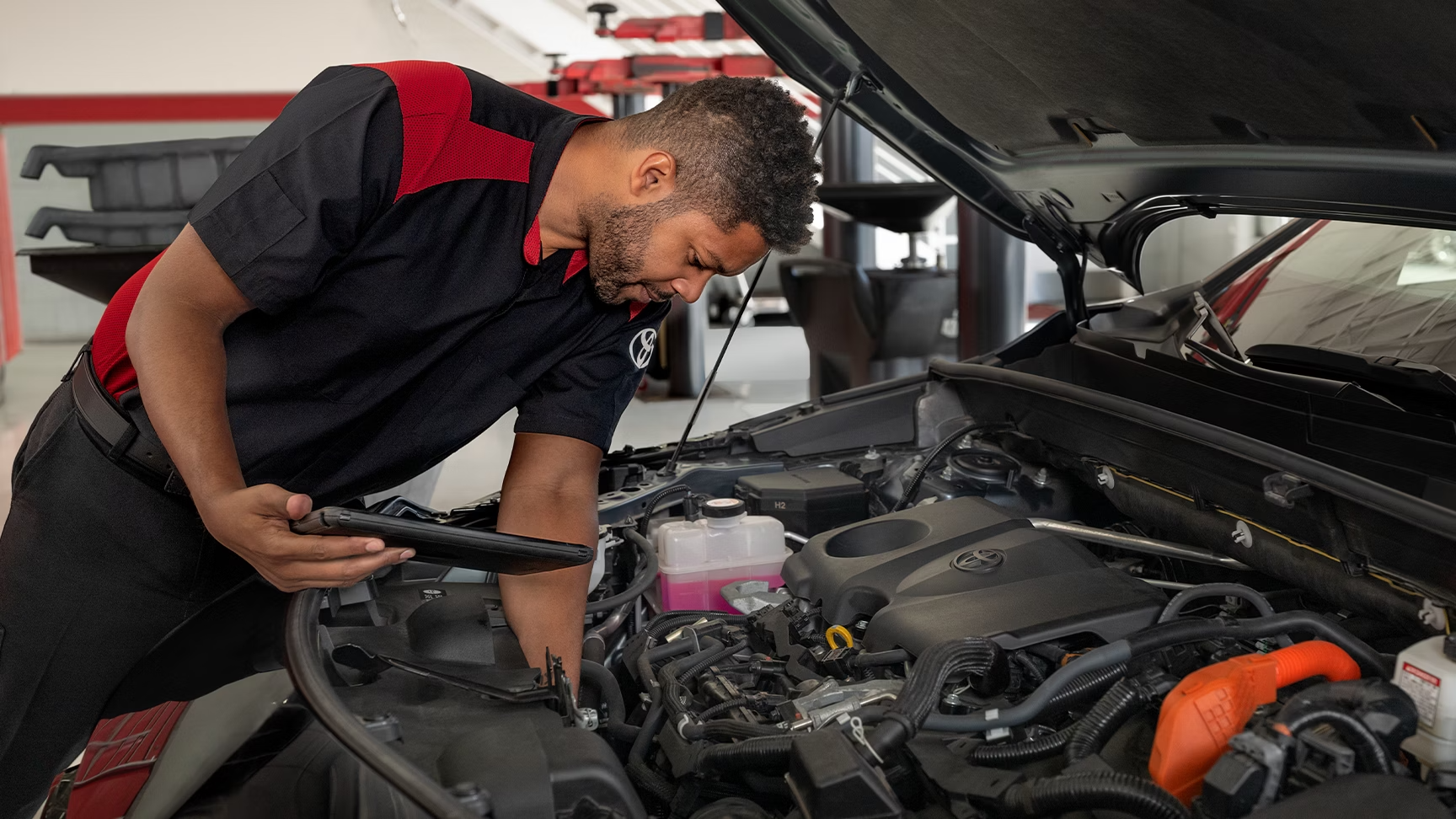 Un técnico de servicio de Toyota realizando tareas de mantenimiento bajo el capó de un vehículo Toyota.