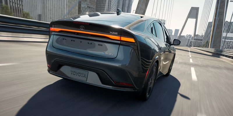 Vista trasera del Toyota Prius Plug-in Hybrid circulando por un puente urbano, en la que se aprecia su elegante diseño y sus luces traseras LED.