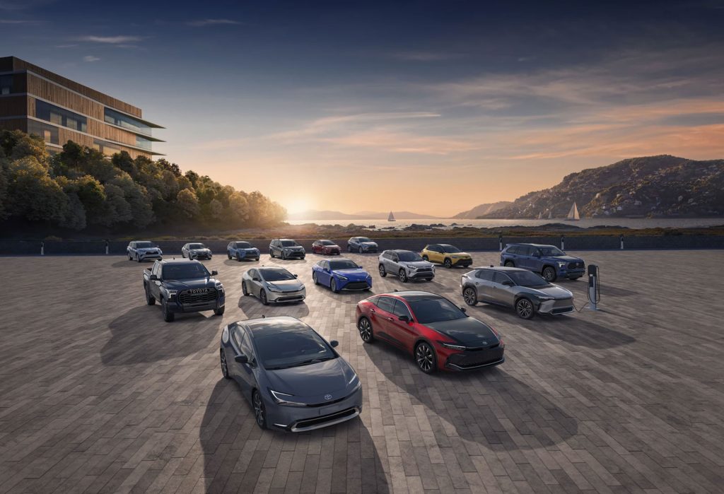 Una gama de vehículos Toyota expuestos en un entorno pintoresco, incluyendo modelos eléctricos y una estación de recarga.