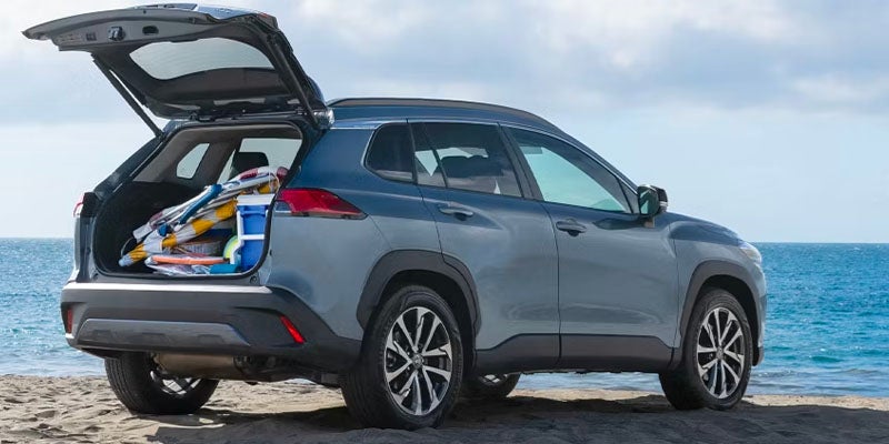 Vista trasera de un Toyota Corolla Cross azul aparcado en la playa con el maletero abierto y lleno de artículos de playa.