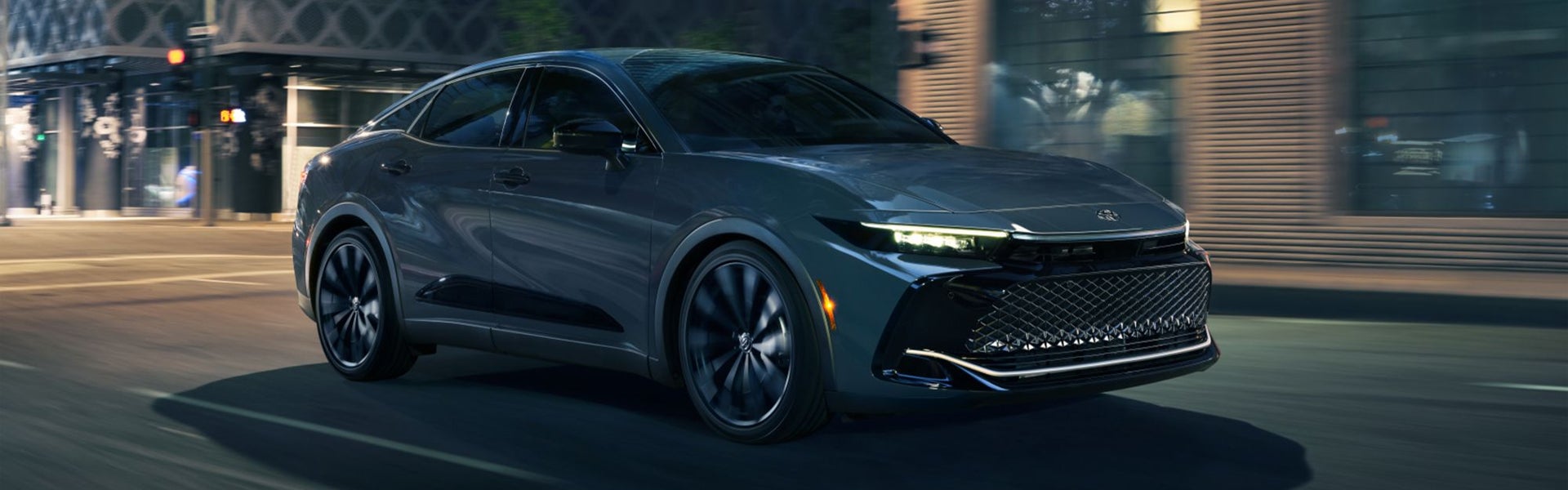 Toyota Crown 2025 circulando de noche por un centro urbano.