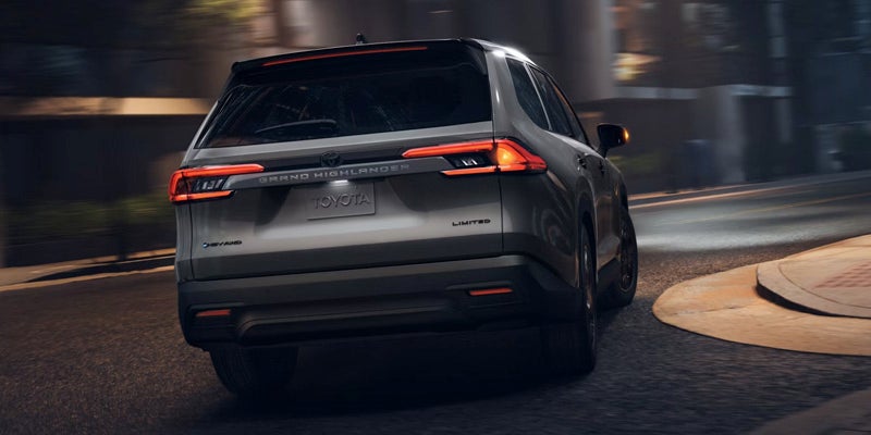 Vista trasera de un Toyota Grand Highlander Hybrid circulando por una calle tranquila al atardecer