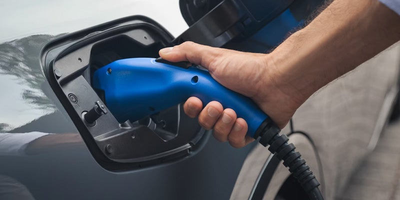 Enchufando a mano un conector azul de recarga de vehículos eléctricos en el Toyota Prius híbrido enchufable de 2025.