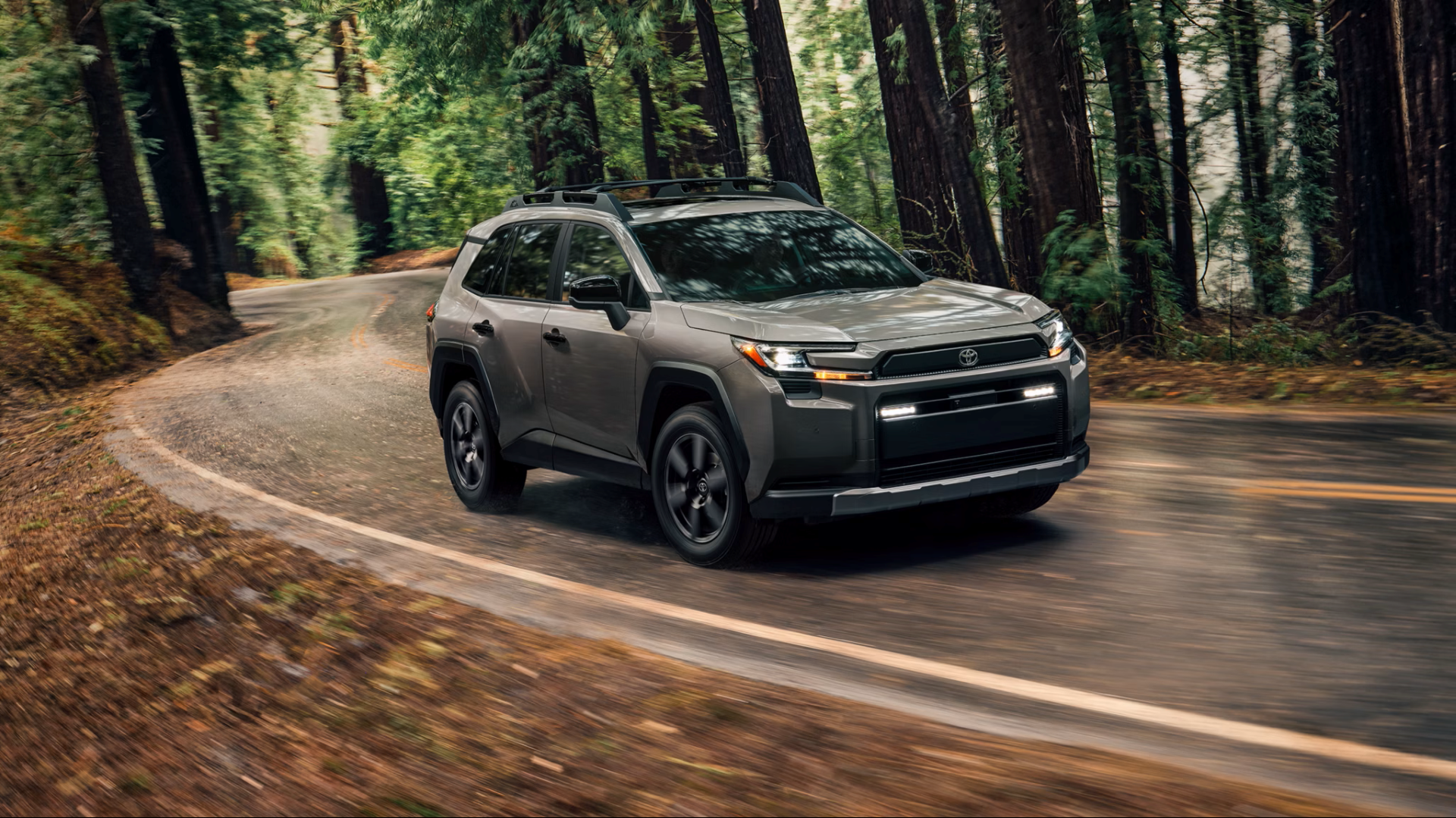 Un Toyota RAV4 gris de 2026 tomando una curva en una carretera forestal